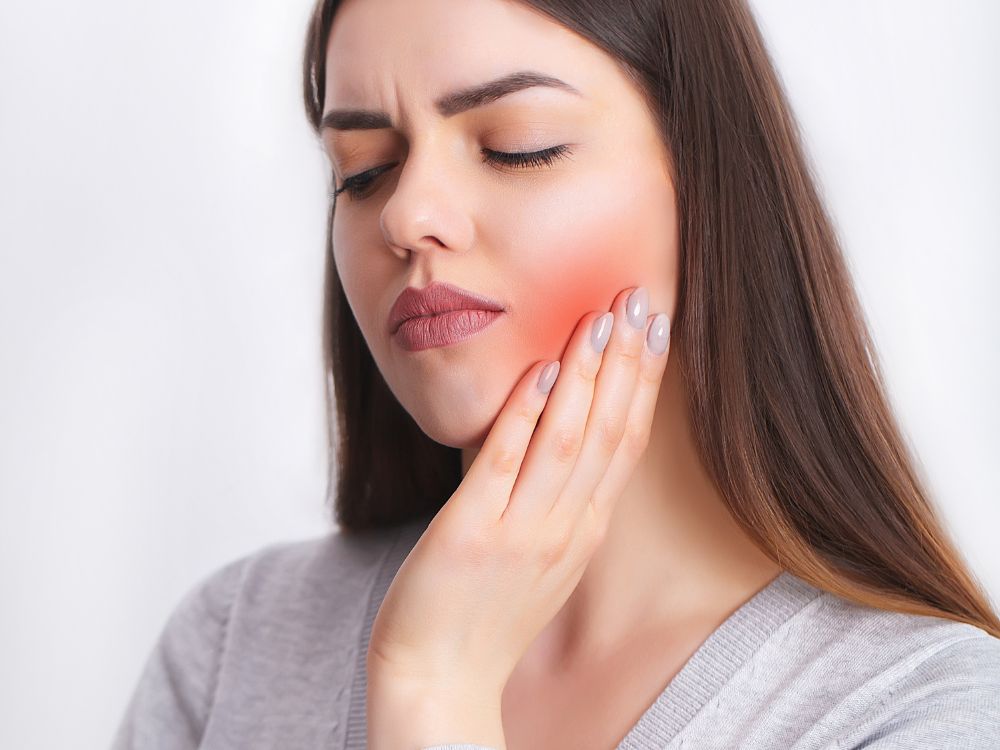 Mulher com dor facial, representando sintomas iniciais da dor neuropática em implante dentário.